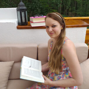 Monika Schulze sitzt auf einem Balkon mit einem Buch in der Handy sie ist Teil der Jury beim tolino media Newcomerpreis 2022