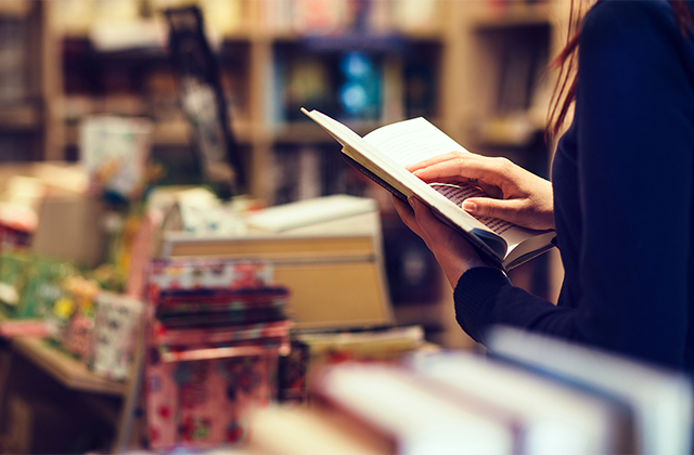 Buchhandel: Person mit offenem Buch in der Hand vor einem Büchertisch in einer Buchhandlung